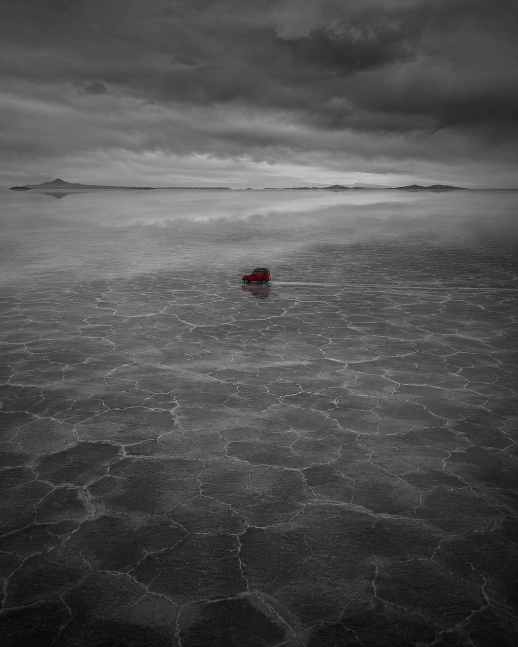 A salt plain under heavy cloud with one small red object at the horizon.