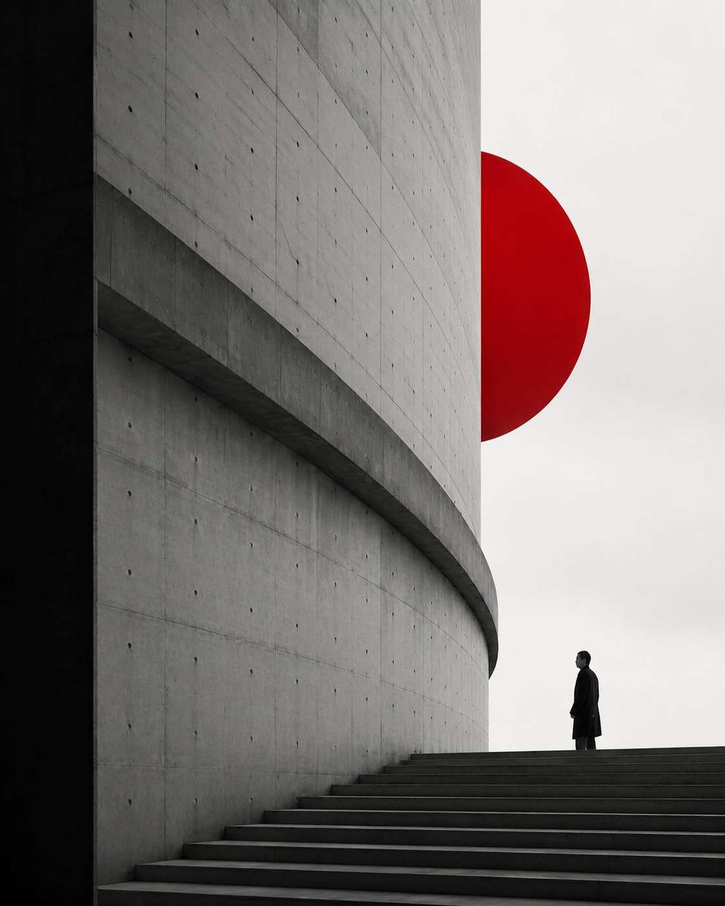A curved concrete wall meeting a deep red disc against a pale sky.