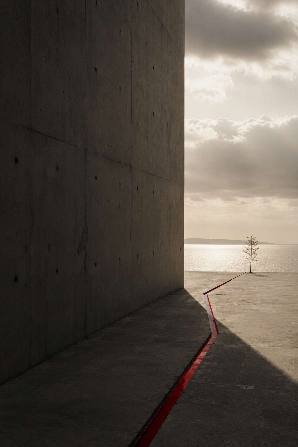 A concrete corridor opening onto a pale sea horizon, one red line on the floor.