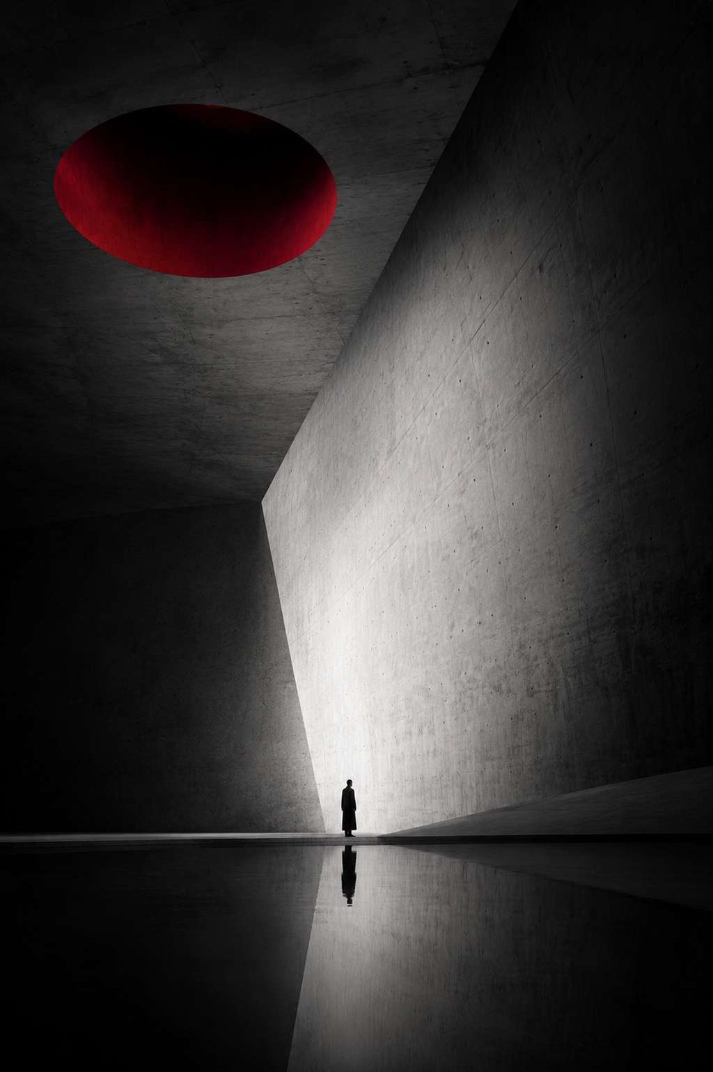 A concrete chamber with a red elliptical opening in the ceiling and a single figure below.